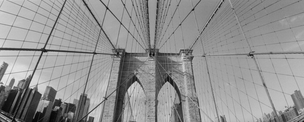 Black and white panoramic photograph of the Brooklyn Bridge tower and suspension cables captured with a Widelux 35mm panoramic film camera in New York City.