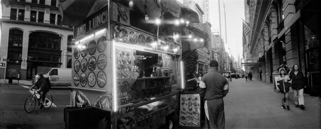 Panoramic photograph of a hotdog stand in New York City shot on a widelux 35mm camera. 