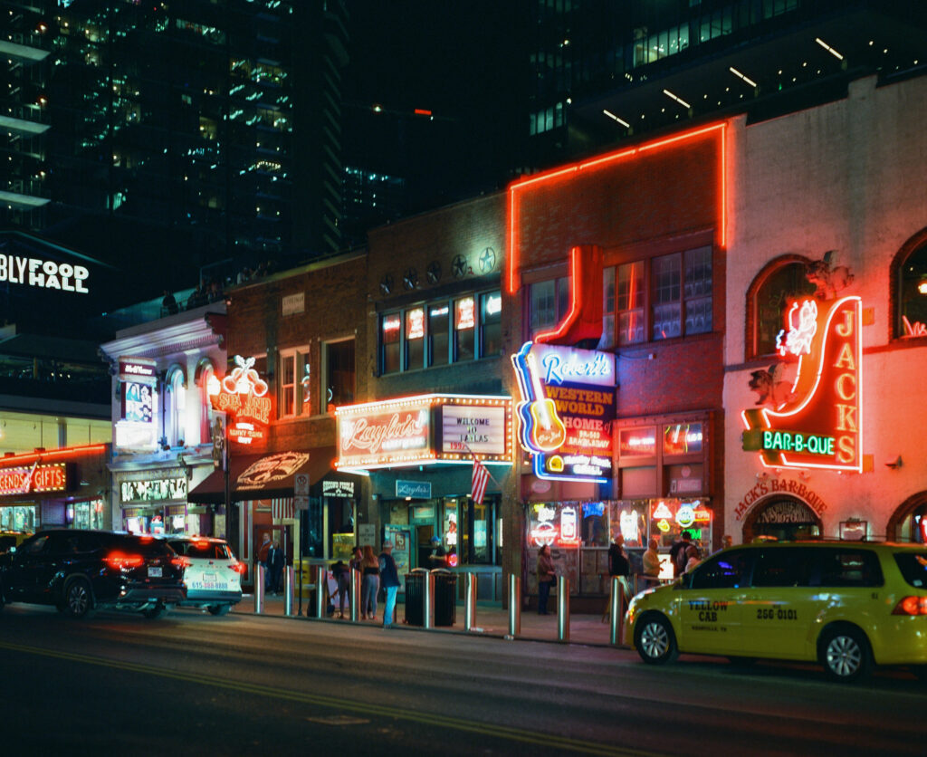 Robert's Western World and Jack's Bar-B-Que illuminated by neon lights on Lower Broadway in downtown Nashville, photographed on Pentax 67 with CineStill 800T film.